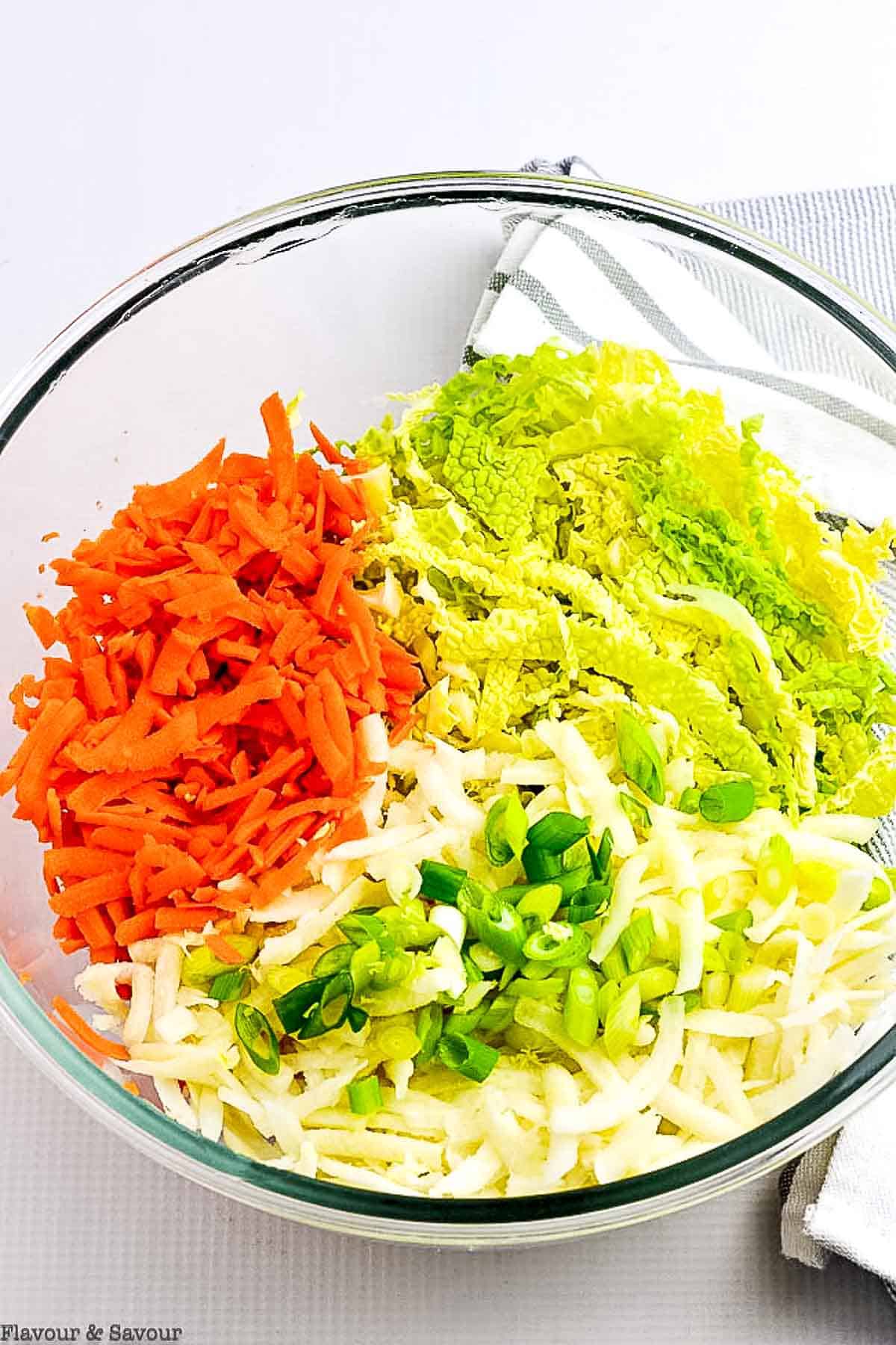 A glass bowl of shredded cabbage, carrots, kohlrabi and green onions.